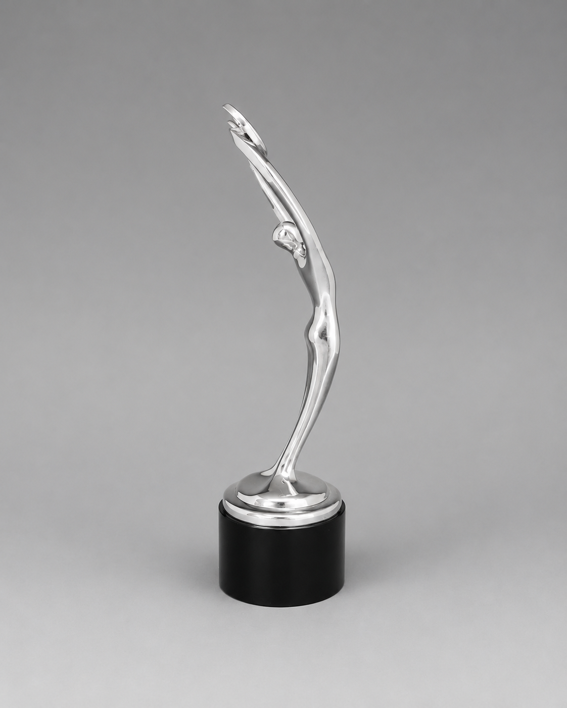 A modern award-style trophy featuring a polished silver abstract female figure sculpture mounted on a glossy black cylindrical base, photographed against a neutral gray studio background.