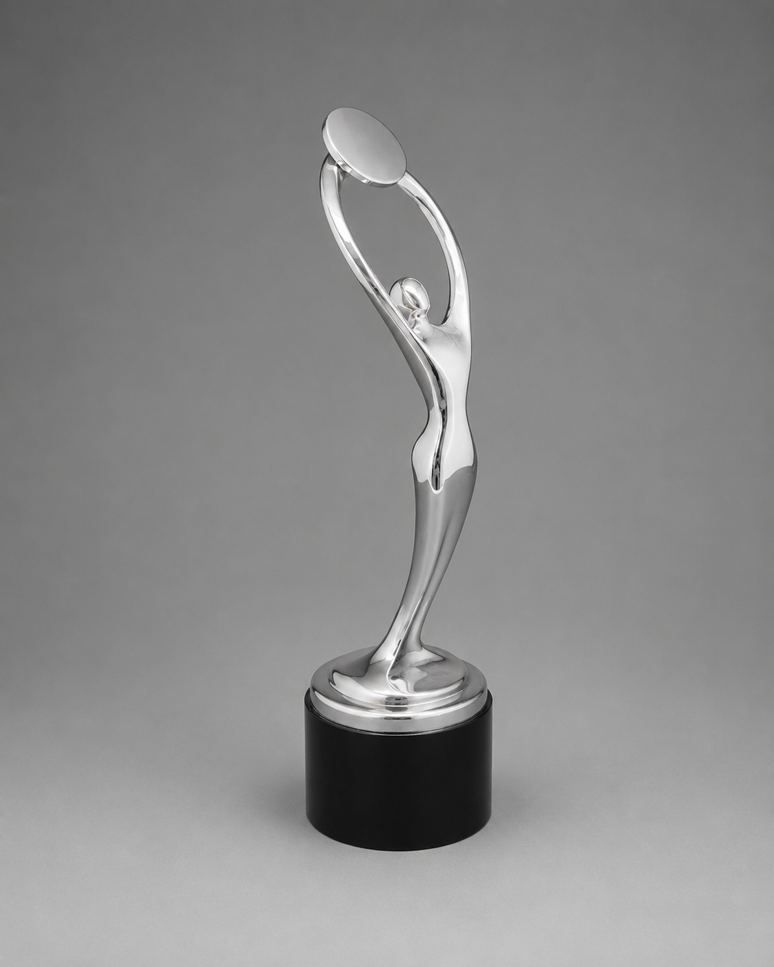A polished silver trophy sculpture of a stylized figure holding a disc above its head, mounted on a round silver platform and a black cylindrical base, photographed against a smooth gray studio background.