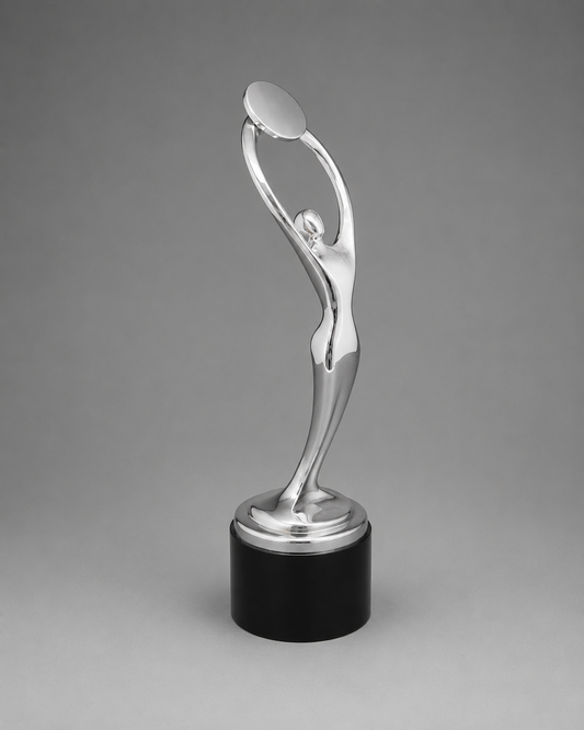 A polished silver trophy sculpture of a stylized figure holding a disc above its head, mounted on a round silver platform and a black cylindrical base, photographed against a smooth gray studio background.