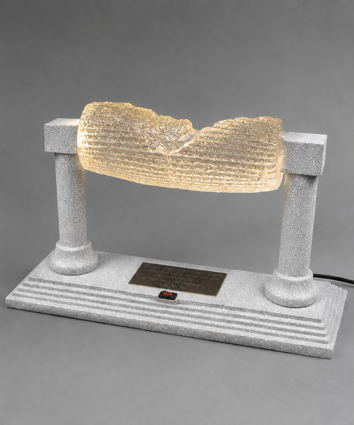 Angled view of glowing Cyrus Cylinder replica on a textured silver base with power cord attached.
