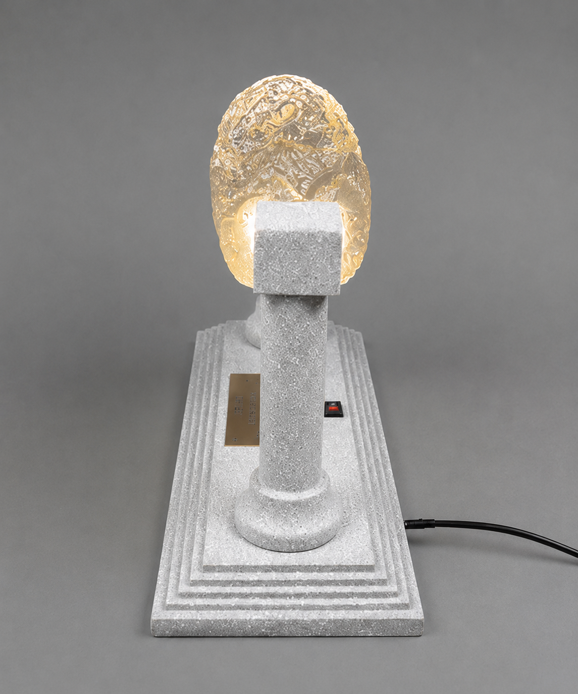 Side view of illuminated Cyrus Cylinder display showing the narrow 5-inch depth and silver support column.