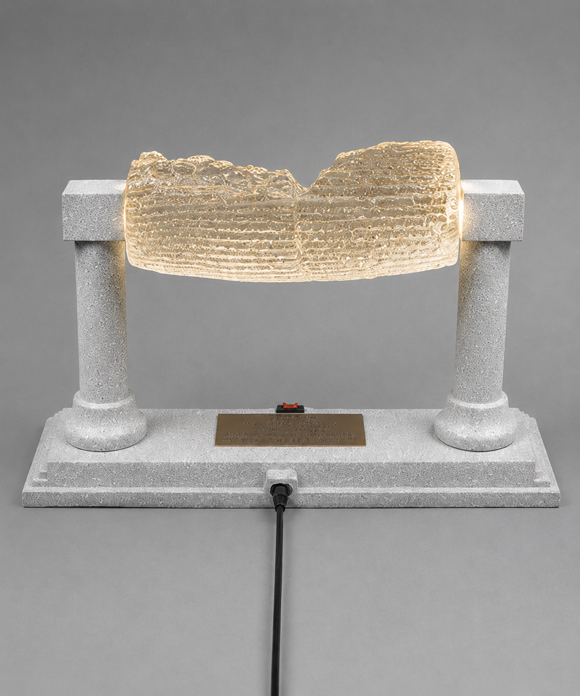 Rear view of glowing Cyrus Cylinder replica with centered power connection and silver display base.