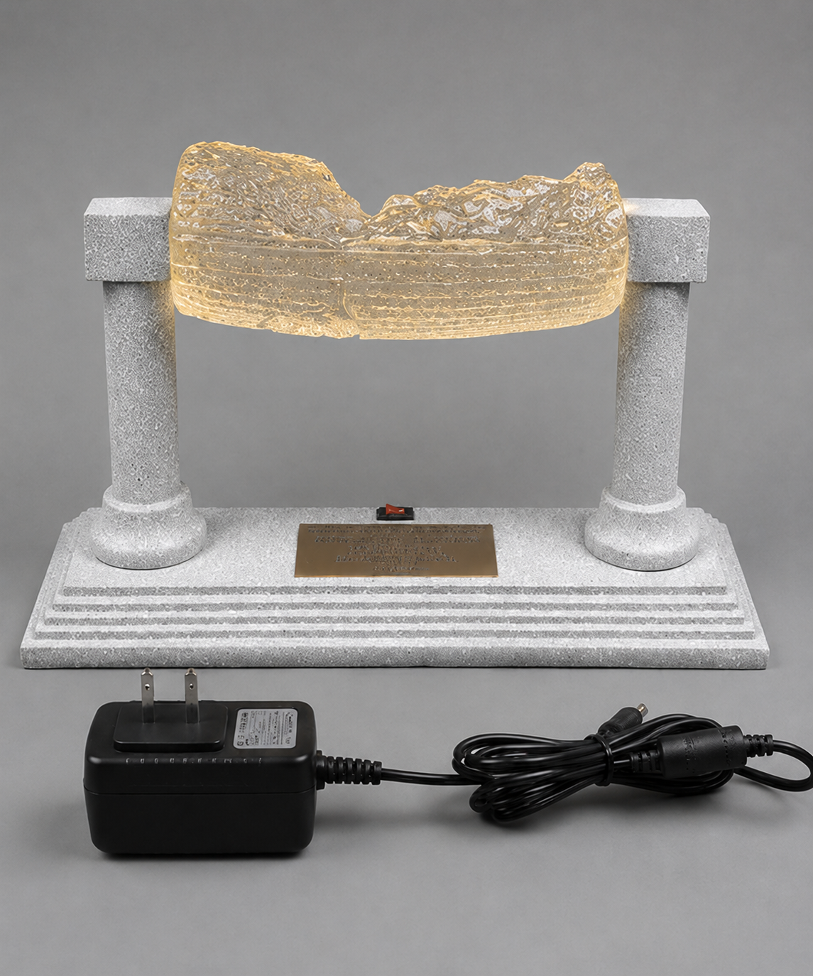 Illuminated Cyrus Cylinder replica with black power adapter and cord displayed in front of the silver stand.