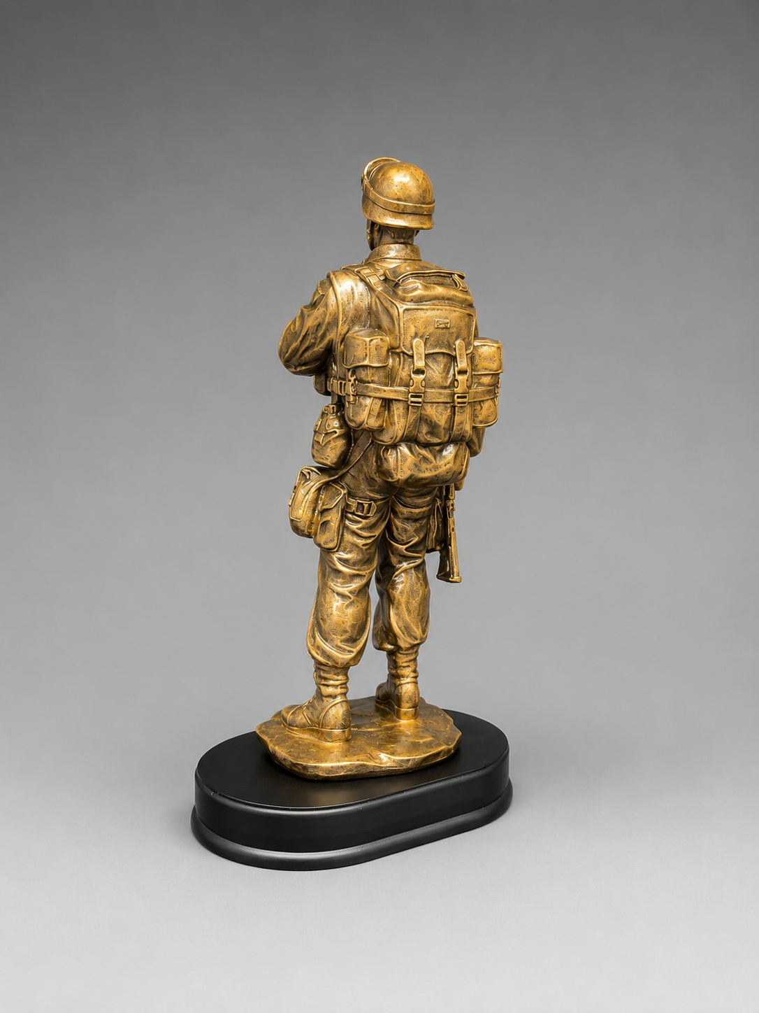 Rear three-quarter view of a bronze soldier statue showing the detailed helmet, backpack, gear, and black display base.