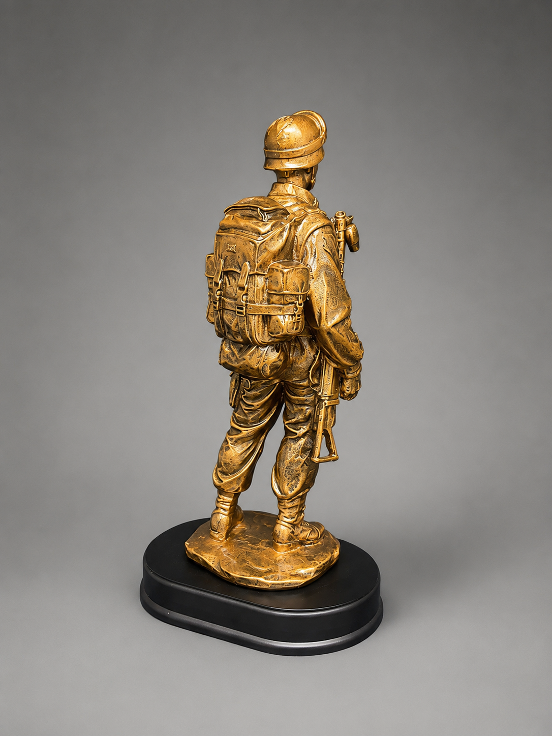 Opposite rear-angle view of the bronze military soldier statue with detailed tactical equipment and rifle on a black oval base.