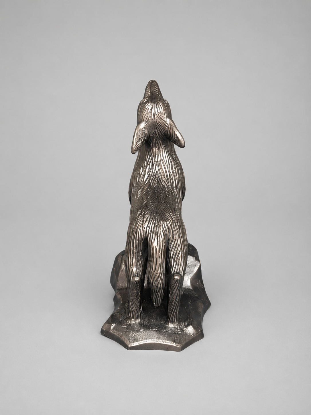 Rear view of a metallic howling coyote figurine, highlighting the textured fur, tail, legs, and sculpted base.