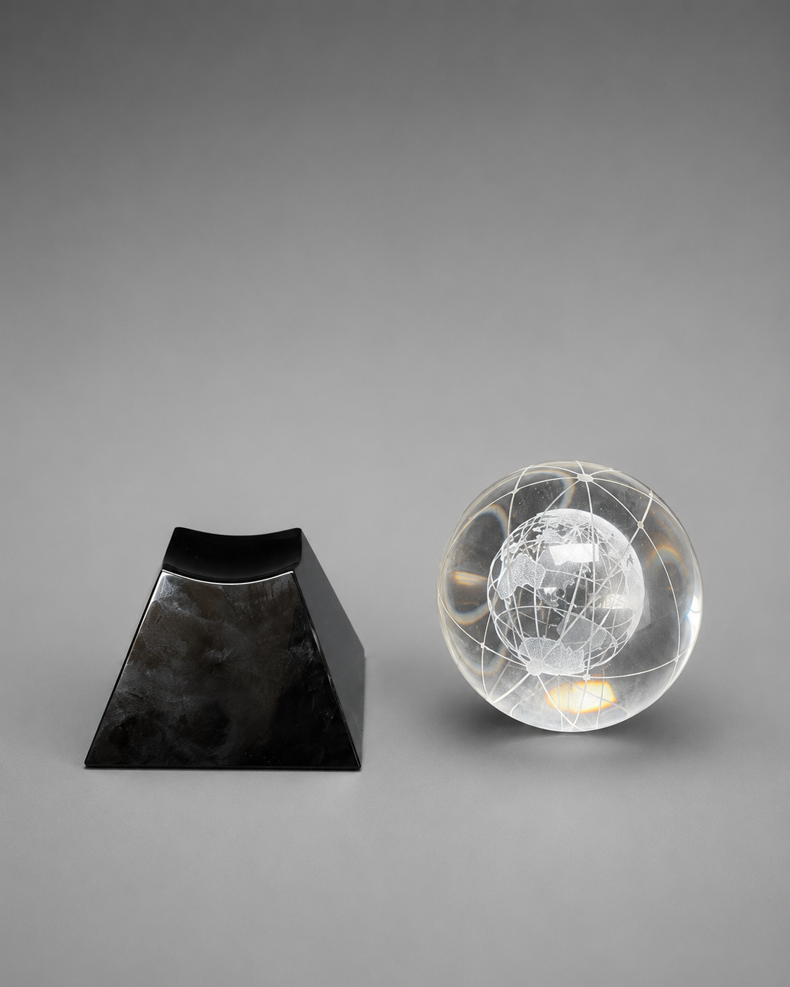 Crystal globe and black pedestal base displayed separately on a neutral gray studio background.