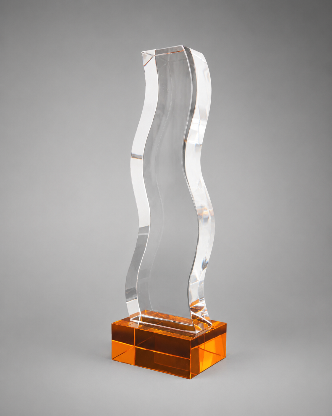 Clear wave-shaped crystal recognition piece on a vibrant bronze/orange rectangular base against a neutral gray background.