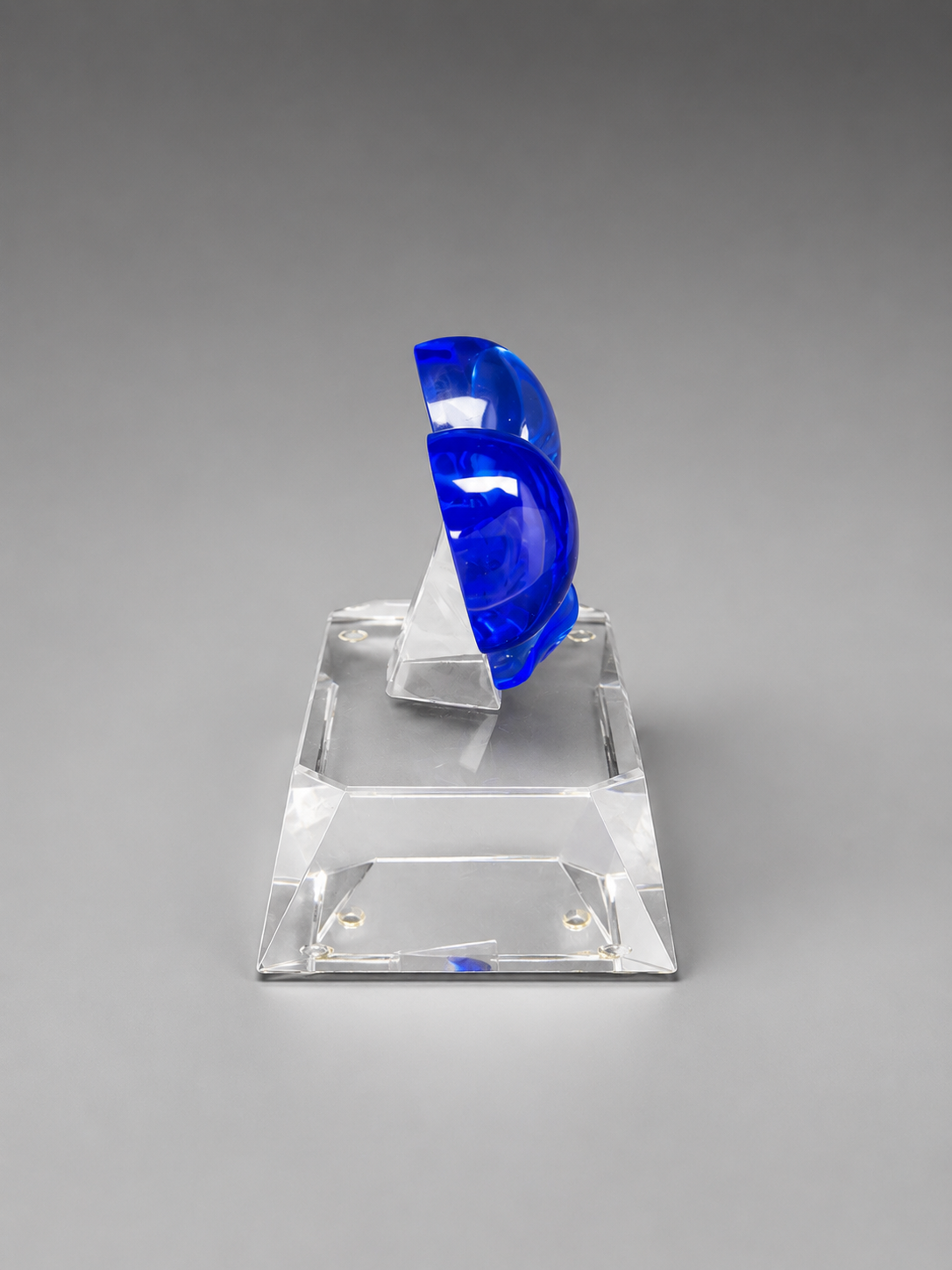 Side profile of a blue crystal bow with a clear support and transparent beveled base on a gray studio background.