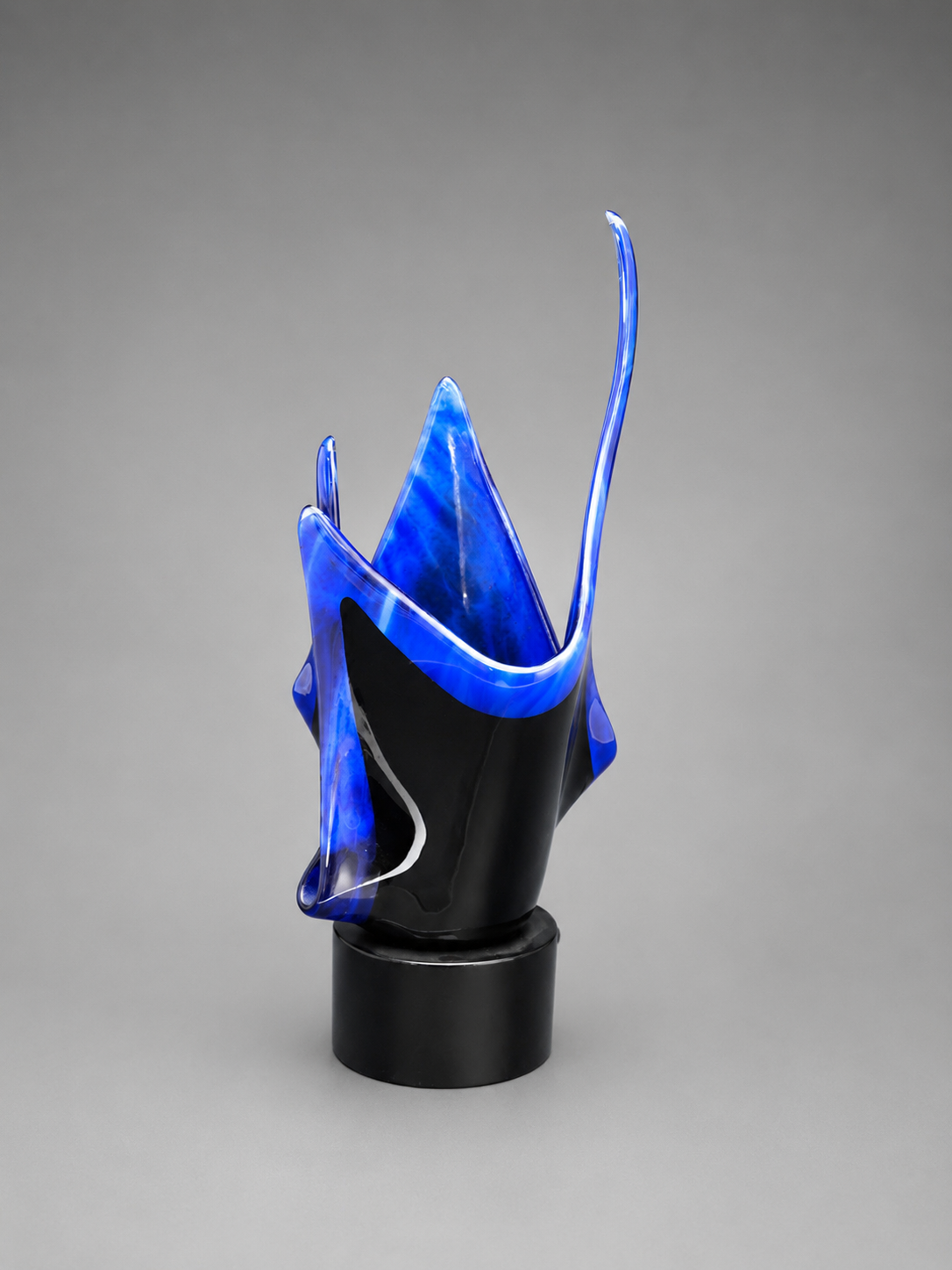 Other side view of blue and black exotic flame designed vase on a black stand.
