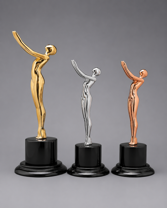 Victory Motion Trophy Collection featuring gold, silver, and rose gold modern figure trophies on glossy black pedestal bases against a neutral gray studio background.