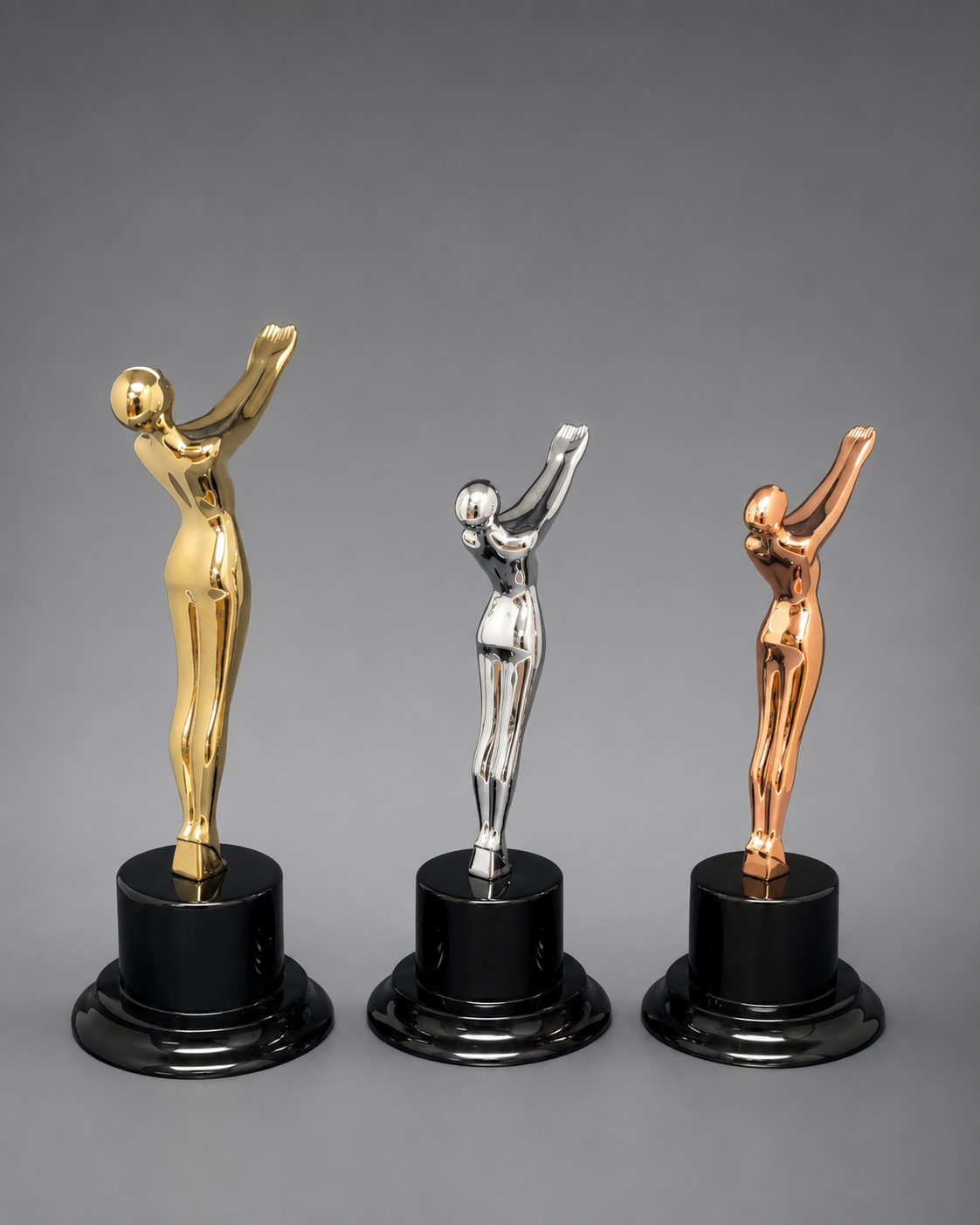 back view of Victory Motion Trophy Collection featuring gold, silver, and rose gold modern figure trophies on glossy black pedestal bases against a neutral gray studio background.