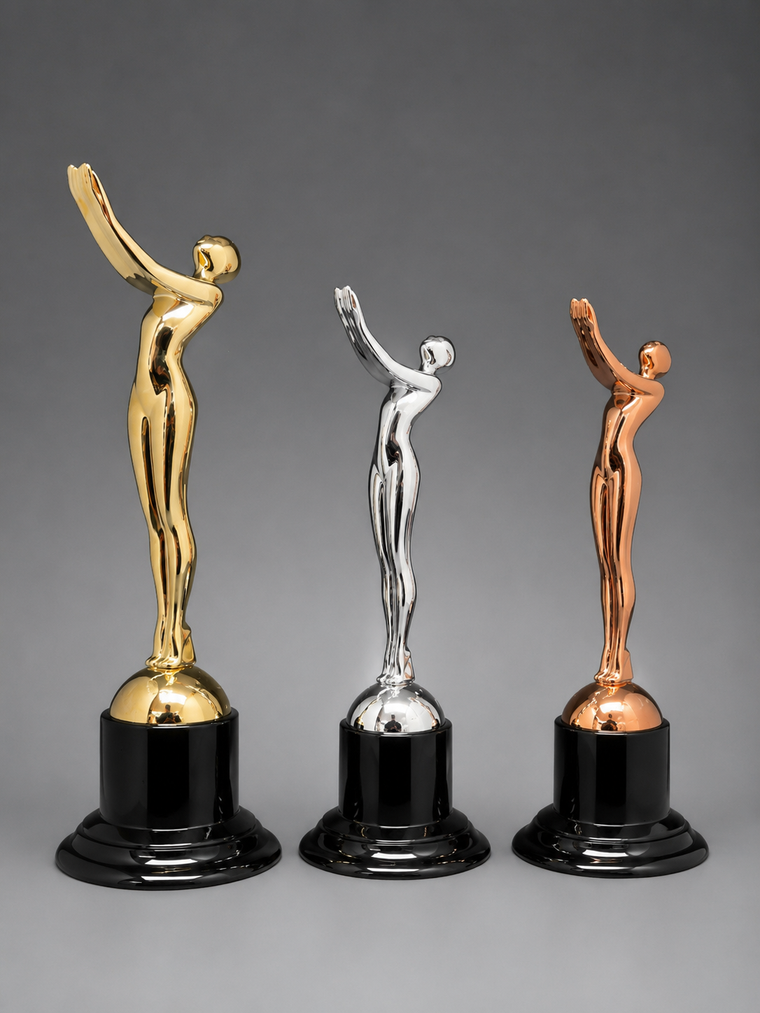 Victory Motion Trophy Collection featuring gold, silver, and bronze trophies with glossy black pedestal bases on a neutral gray studio background.