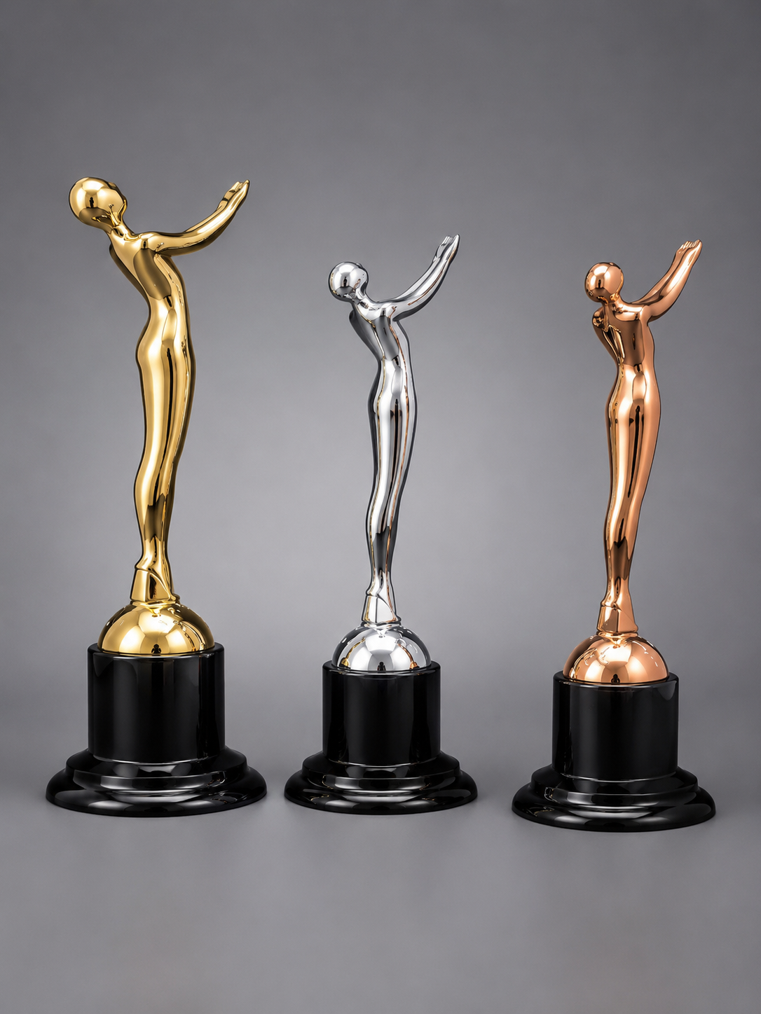 Rear view of the Victory Motion Trophy Collection in gold, silver, and bronze finishes with black pedestal bases on a professional gray studio background.