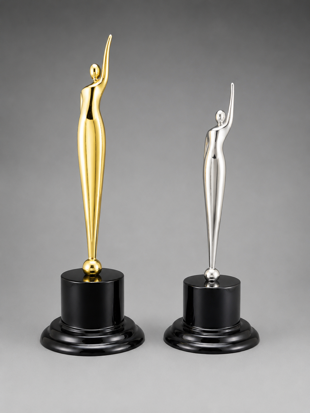 Gold and silver abstract achievement awards displayed side by side on glossy black pedestal bases against a neutral gray studio background.