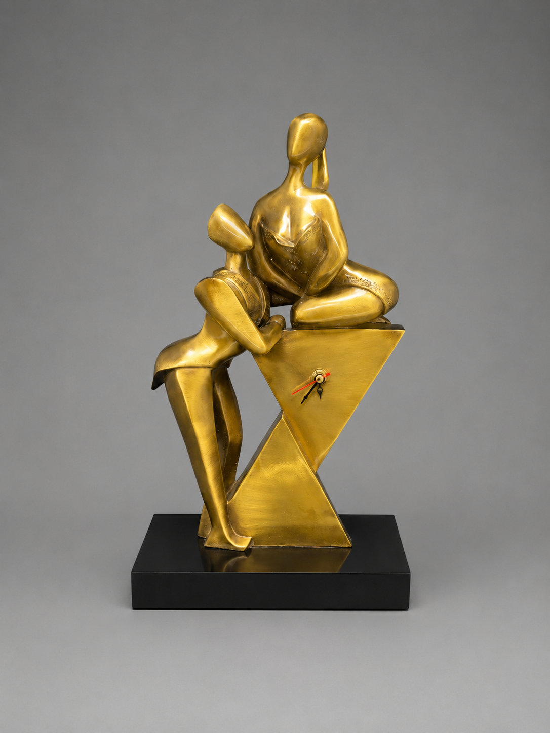 Gold sculpture of two abstract figures on a black base against a gray background