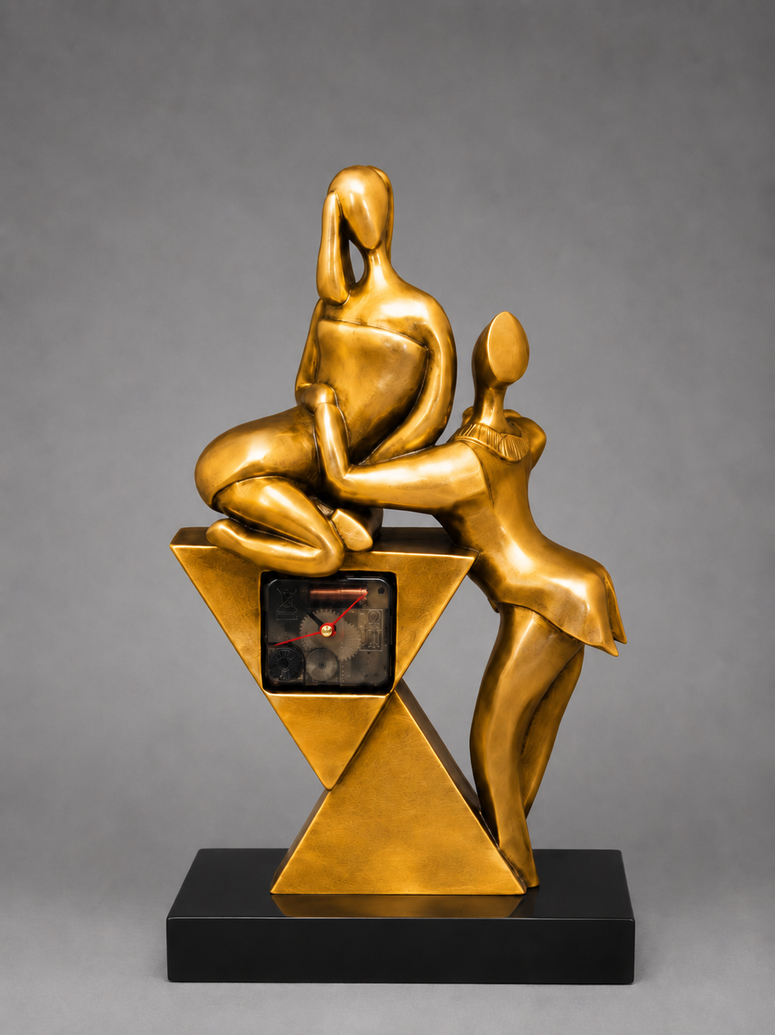 Gold sculpture of two figures on a geometric base with a clock, against a gray background