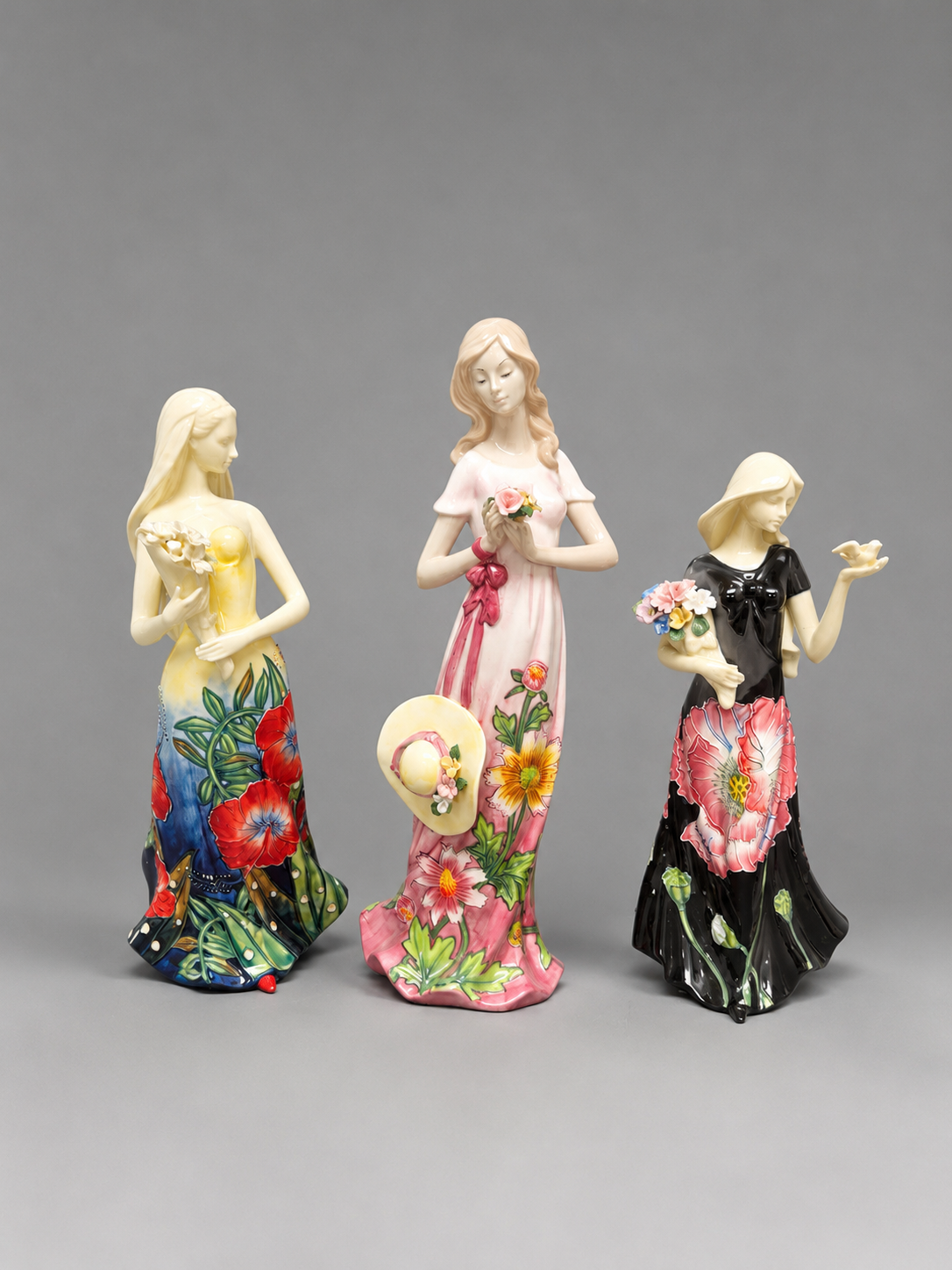 Three colorful figurines of women with floral designs on a gray background
