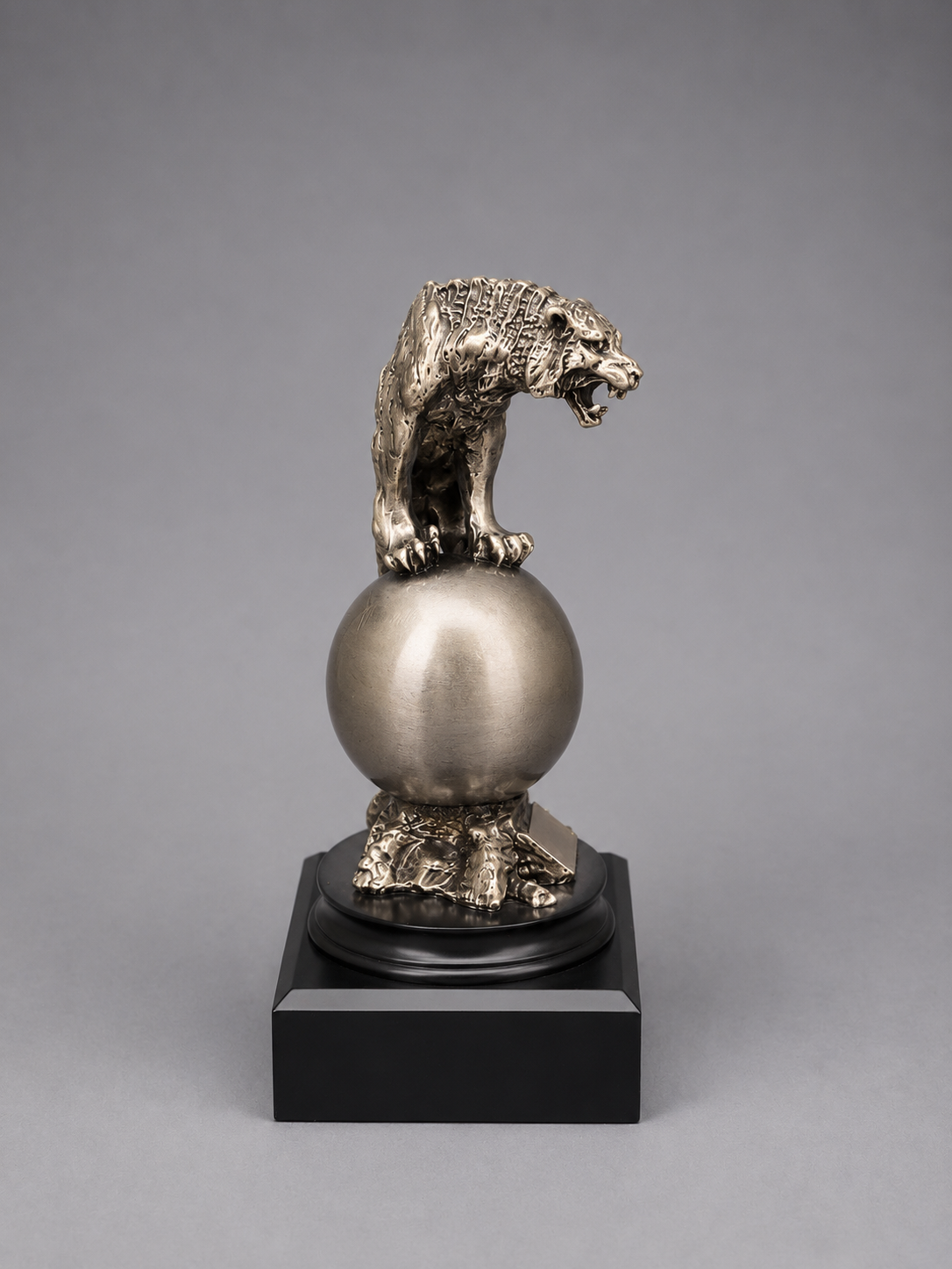 Silver tiger on top of a sphere on a gray background