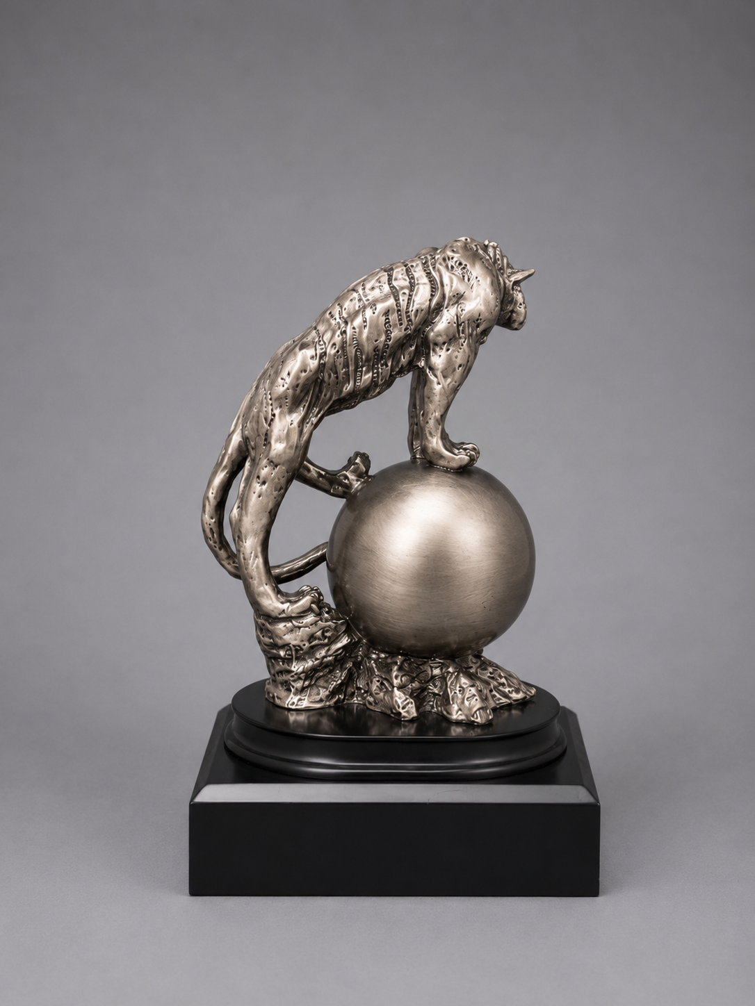 silver sculpture of a tiger on a sphere with a gray background