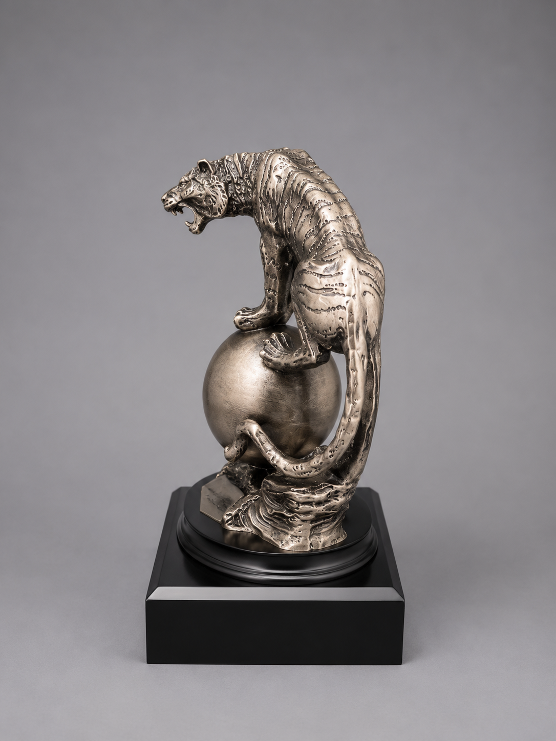 silver sculpture of a tiger on a sphere with a gray background