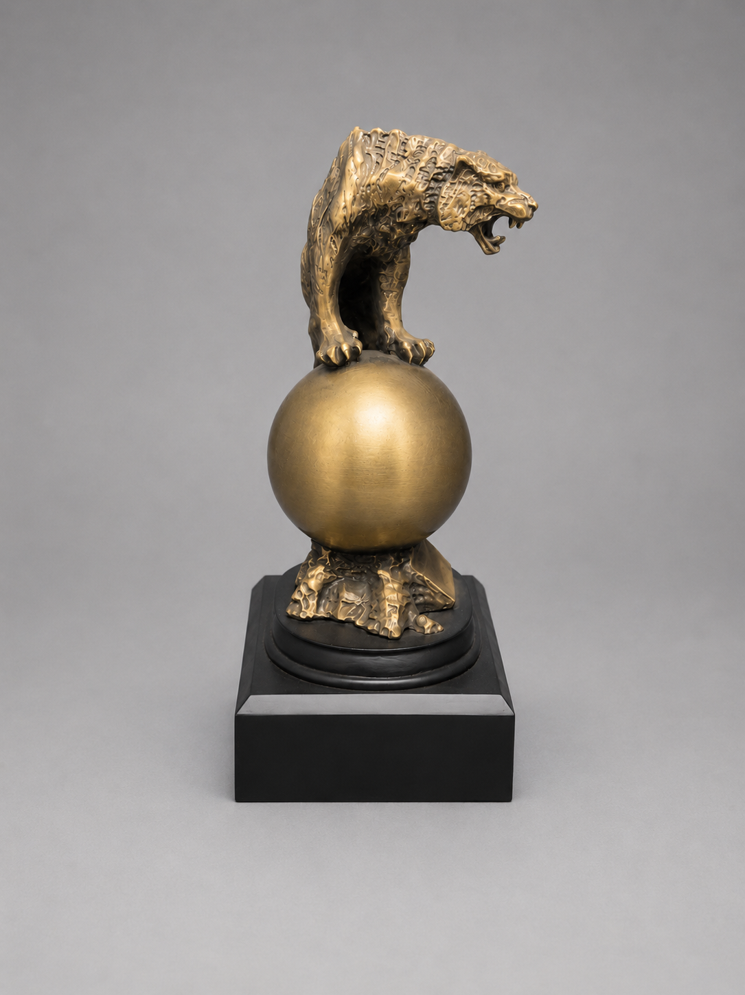Bronze statue of a tiger on a sphere with a black base against a gray background