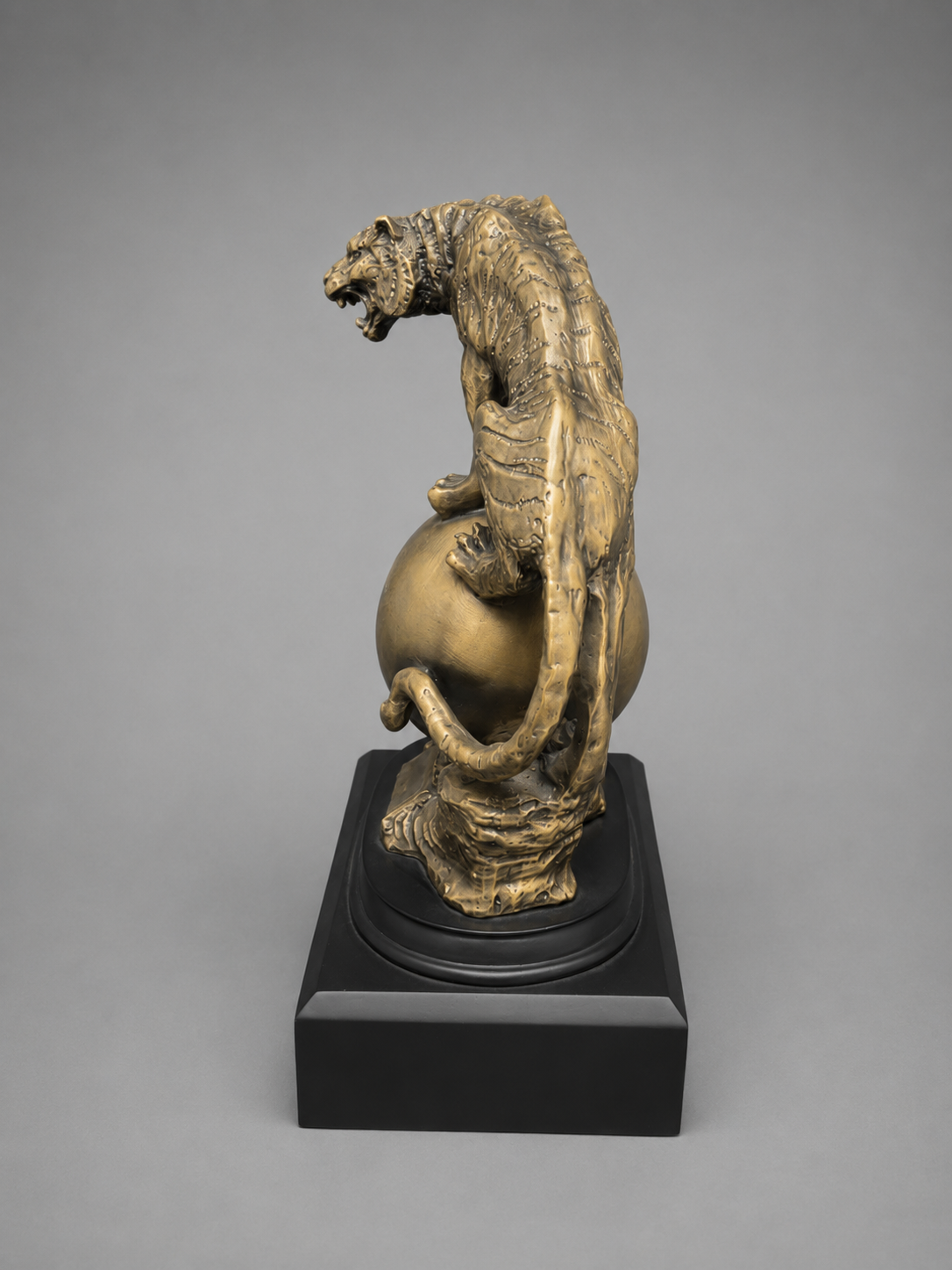 Bronze sculpture of a tiger on a sphere on a gray background