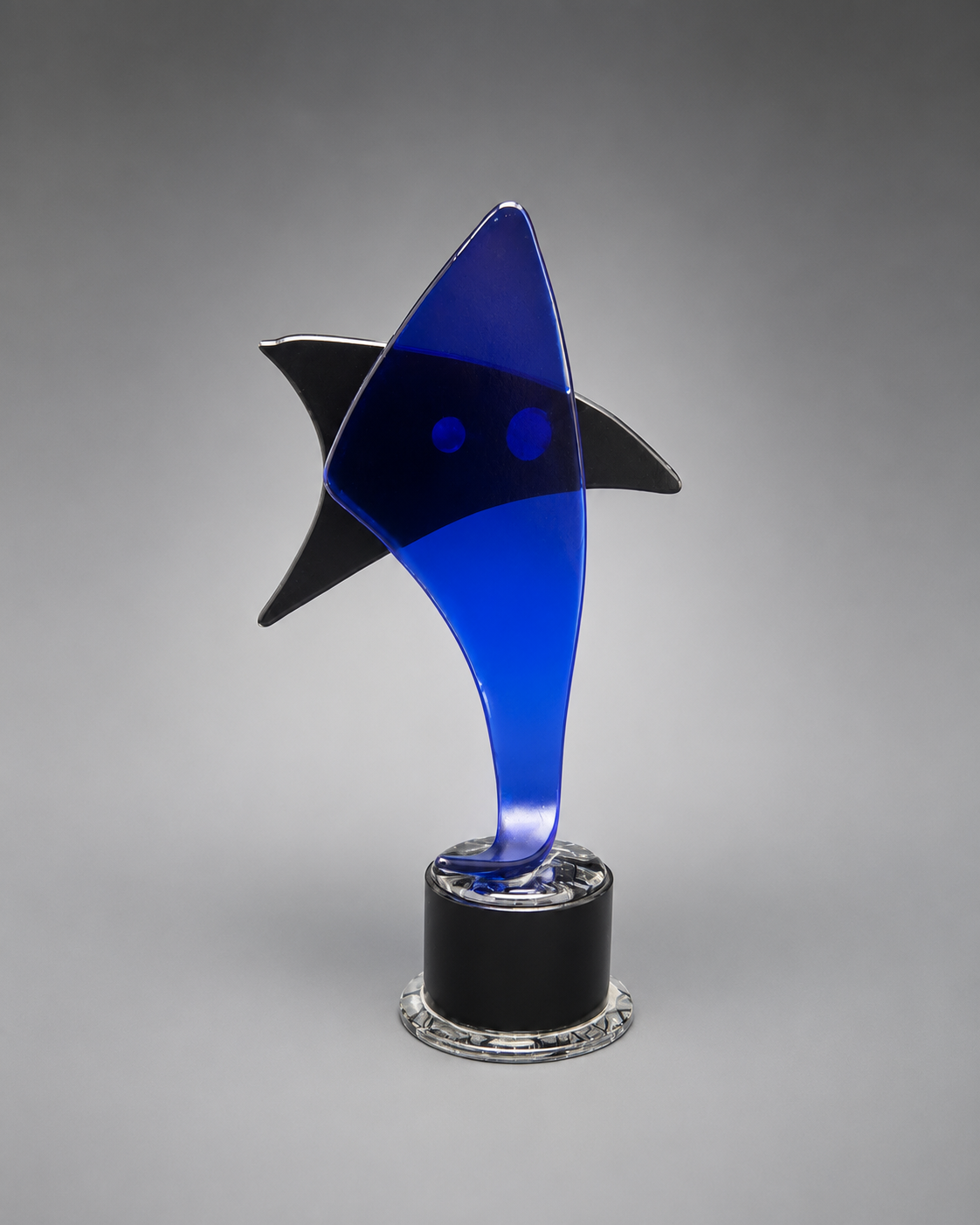 back view of A modern abstract shark-shaped glass award trophy with a vibrant blue body, black fins, and a clear circular base, photographed on a neutral gray gradient background.