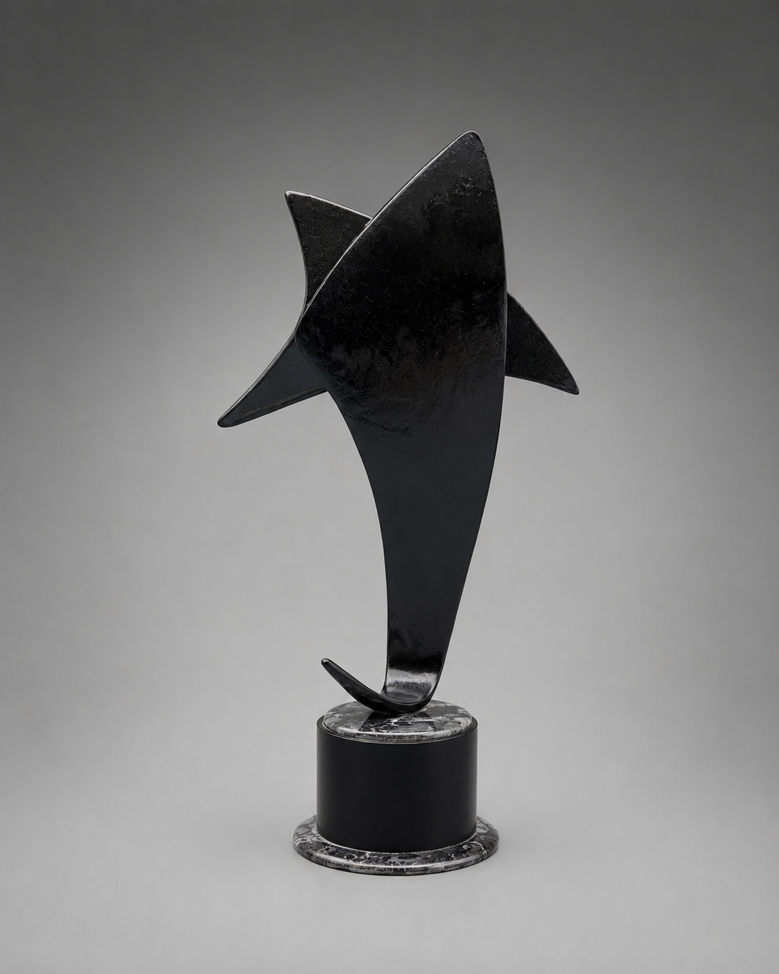 back view of A black trophy plaque  sculpture mounted on a cylindrical black base with a textured gray circular ring, photographed against a smooth gray studio background.