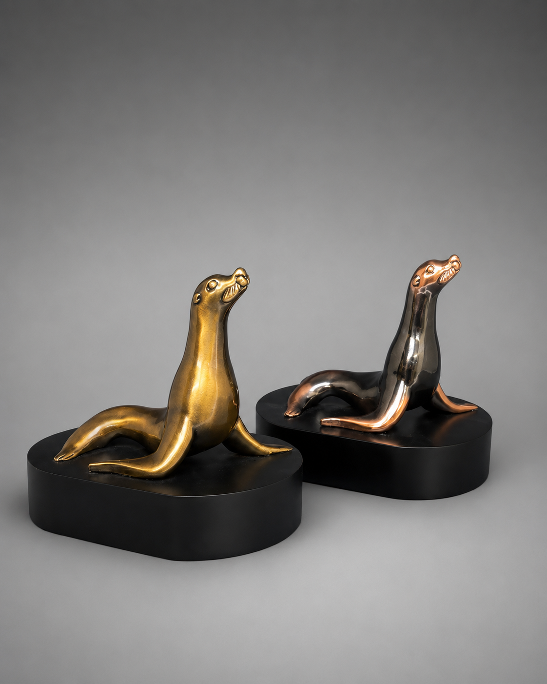 Two bronze seal sculptures on black bases against a gray background