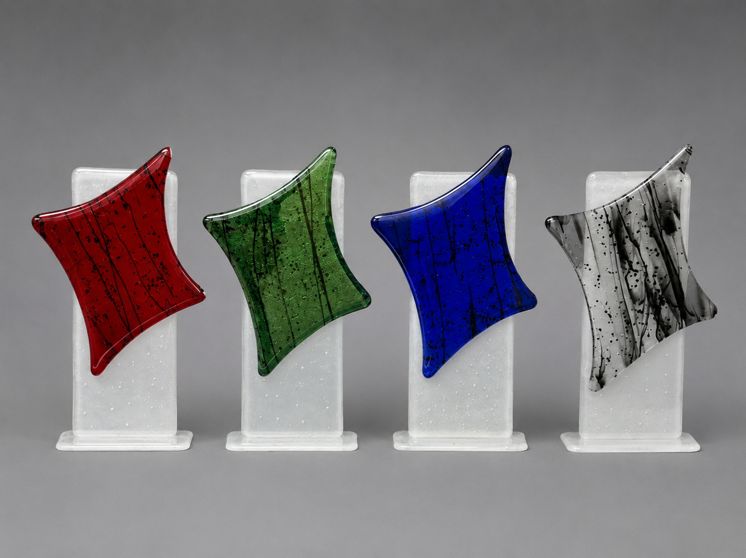 Four colorful glass pieces on white stands against a gray background