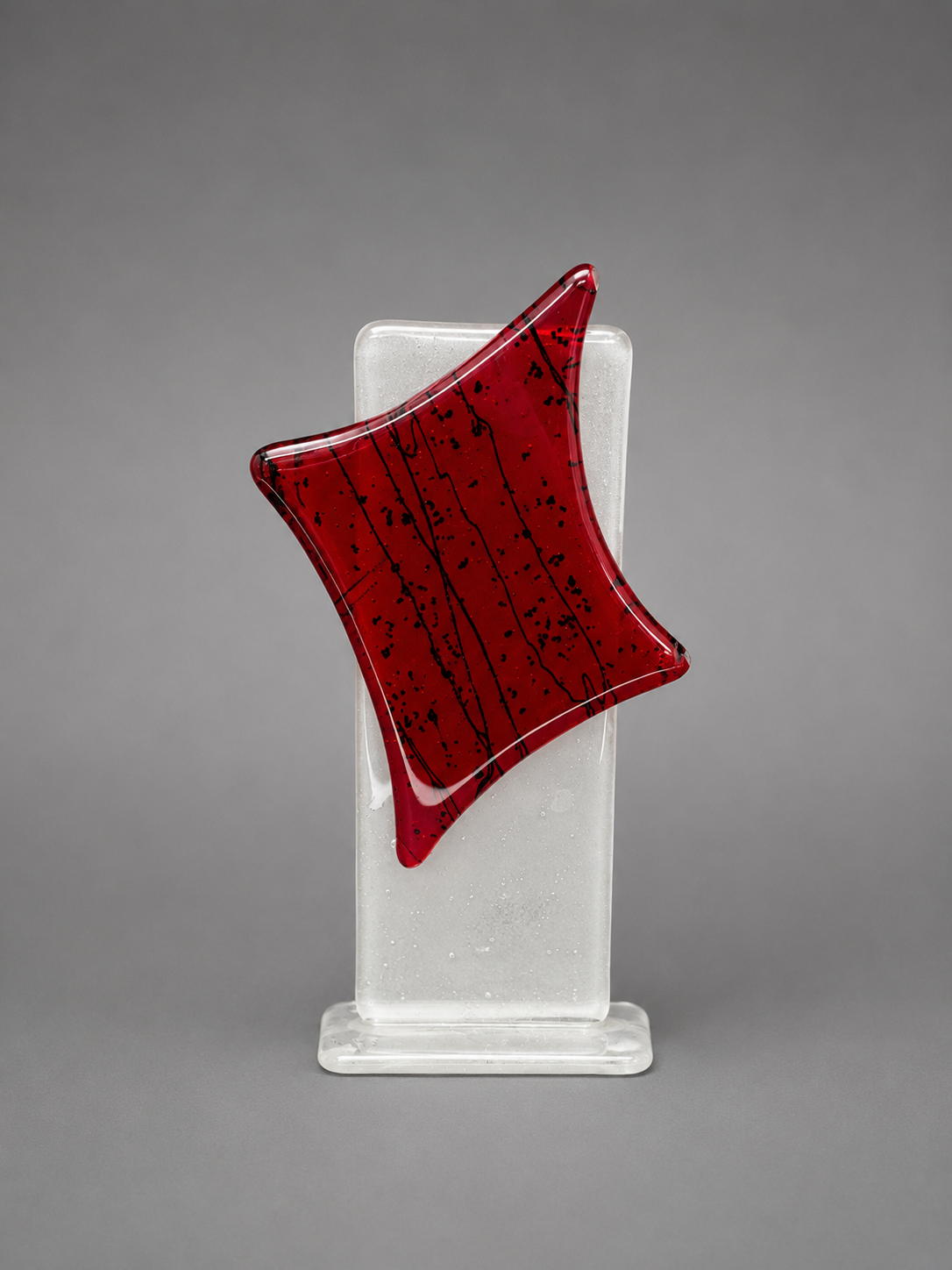 Red glass sculpture on a clear stand against a gray background