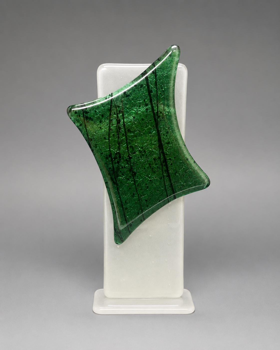 Green glass sculpture on a white stand against a gray background