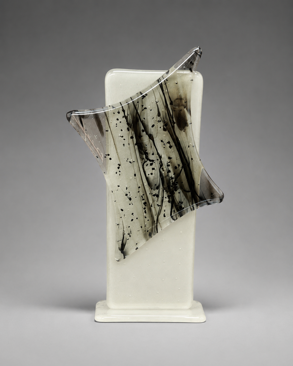 Glass sculpture with black speckled pattern on a gray background