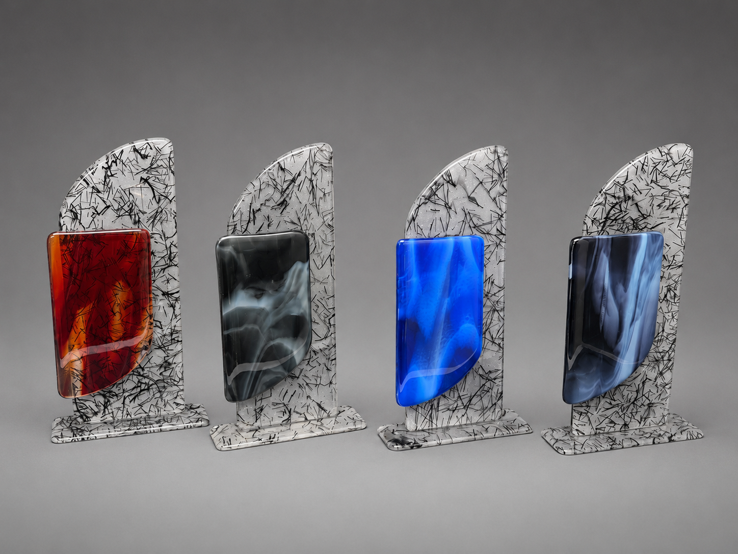 Four decorative glass art pieces with white and black marbled bases and vertical colored inserts, shown on a neutral gray background. The inserts are colored in amber-red, black, bright blue, and dark navy.