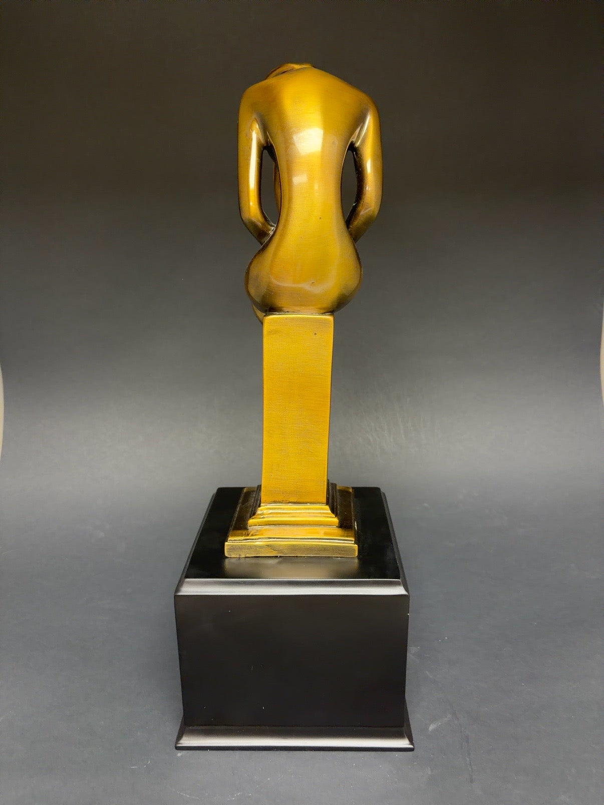 Gold statue on a black base against a gray background