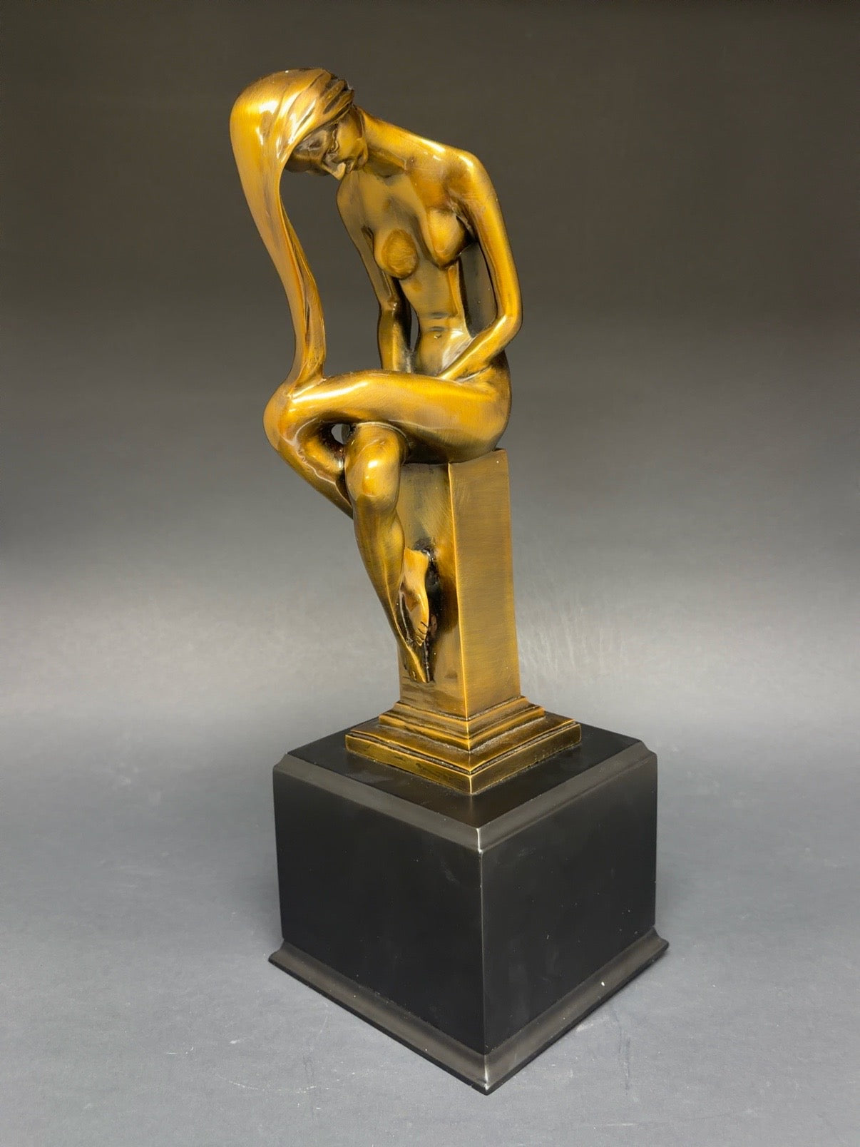 Gold sculpture of a nude figure on a black base against a gray background